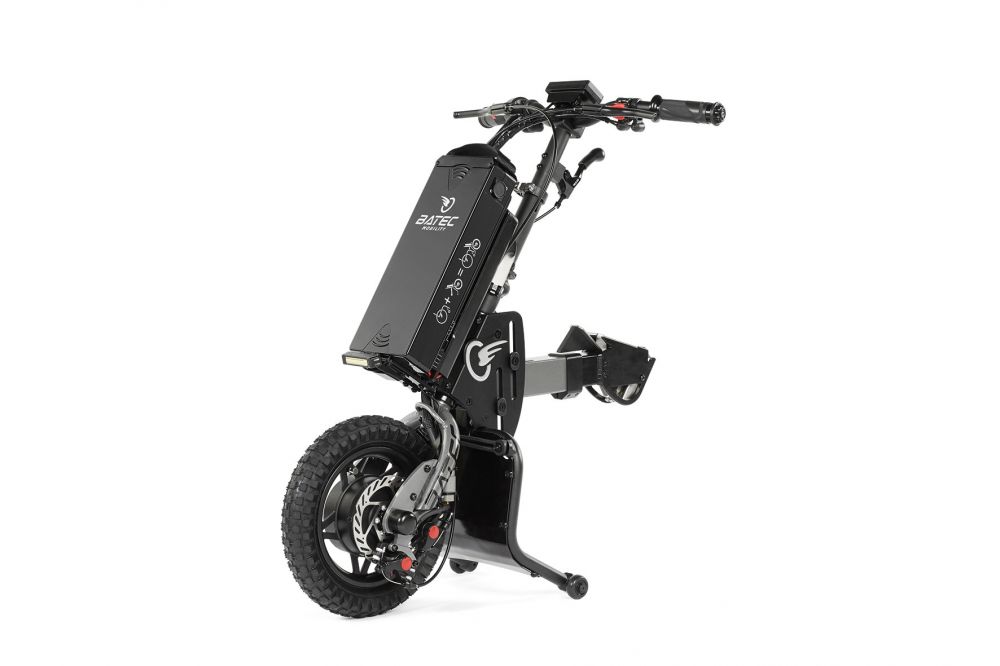 Das Bild zeigt das Rollstuhlzuggerät BATEC MINI 2 als Freisteller auf einem weißen Hintergrund. Zu sehen ist das Zuggerät selbst, die Lenkeinheit, der Akkupack, das grobstollige Antriebsrad, sowie der einzigartige Mudguard und die Dockingbar zur Befestigung am Rollstuhl. Das Gerät hat die Farben Schwarz und Grau.   