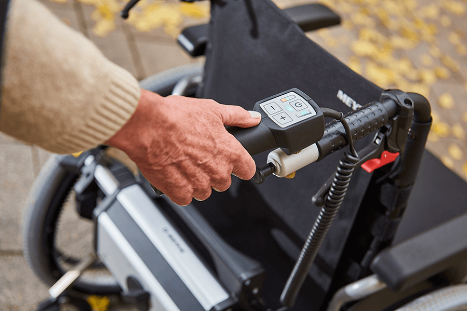 Das Bild zeigt eine Detailaufnahme vom Handgriff, über welchen der Rollstuhlantrieb V-MAX2 bedient wird. Zu sehen ist die Hand einer älteren Frau, die mühelos und einfach alle Funktionen der Schiebe- und Bremshilfe erreichen kann.