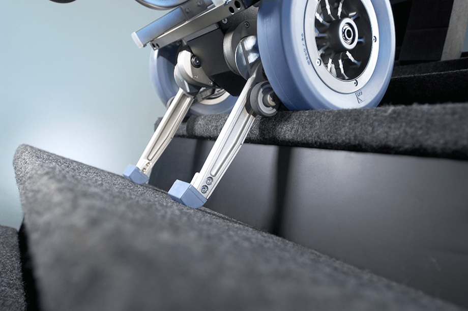 Das Bild zeigt den Steigvorgang der Treppenhilfe c-max. Die Steigbein sind ausgefahren und setzen bereits auf der unteren Treppenstufe auf. Die Sicherheitsbremsen, welche am großen Laufrad befestigt sind, setzen am Stufenrand auf und schützen so vor einem abwärtsrollen.